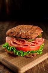 resh sandwich with ham, cheese, bacon, tomatoes, salad, cucumbers and onions on a wooden cutting Board