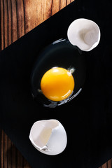 Raw broken egg and shell on black cutting Board on wooden table