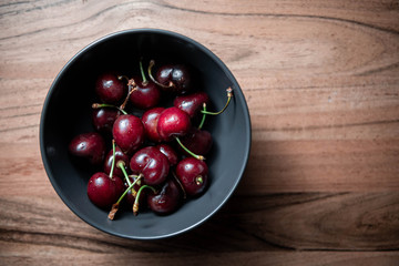 A bowl of cherries on a wooden table.