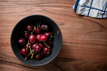 A bowl of cherries on a wooden table.