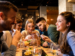 Group of young friends having fun in restaurant, talking and laughing while dining at table.