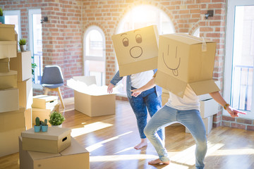 Crazy couple wearing cardboard boxes with funny emoji faces over head, having fun at new house