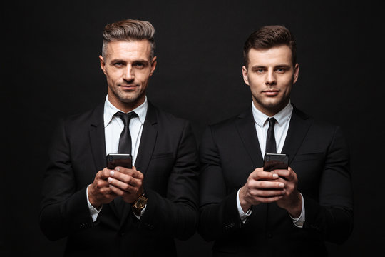Adult business men posing isolated over black wall background using mobile phones.