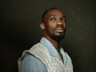 Young man as a medieval grandee or nobleman on dark studio background. Looking serious. Portrait of...