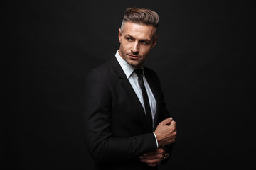 Handsome mature business man posing isolated over black wall background.