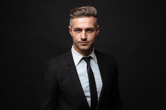 Handsome mature business man posing isolated over black wall background.