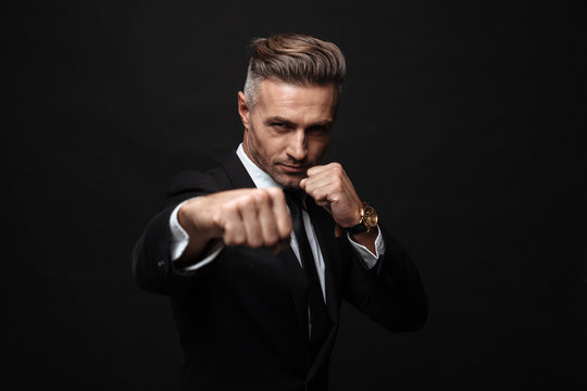 Mature business man posing isolated over black wall background boxing.