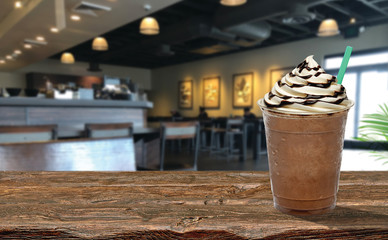 Frappuccino with cream and chocolate sauce in takeaway cup on wooden table at cafe