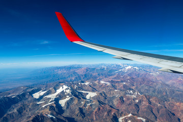 Wing of an airplane flying above the morning clouds and Andean mountain range