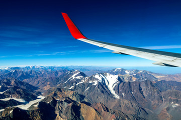 Wing of an airplane flying above the morning clouds and Andean mountain range