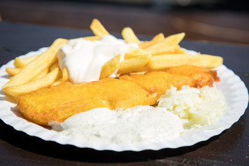 Seelachs Backfisch im Bierteig mit Remoulade, Pommes, Mayonnaise und Krautsalat draußen auf Pappteller und Holztisch 