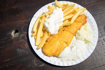 Seelachs Backfisch im Bierteig mit Remoulade, Pommes, Mayonnaise und Krautsalat draußen auf Pappteller und Holztisch 