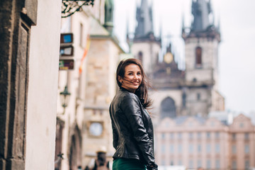 Fototapeta premium Street portrait of adorable brunette woman with long hair posing at Old Town Square in Prague. smiling pretty brunette girl, lifestyle. observatory of astronomical clock tower in Prague, Czech