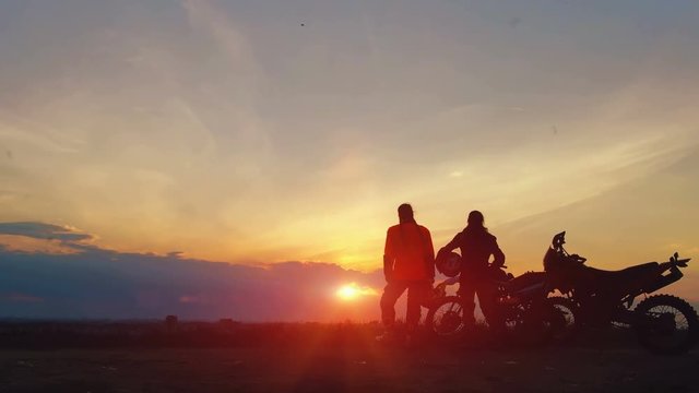 Silhouettes two riders with their bikes greet each other with victory. Silhouettes of motorcycles and riders on the background of beautiful sunset. Enjoy the freedom. Enduro.