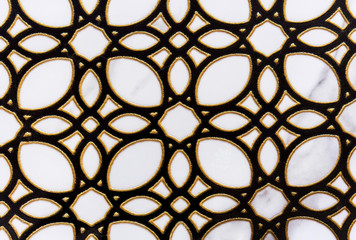 Black openwork ornament with a gold border on a white ceramic tile.