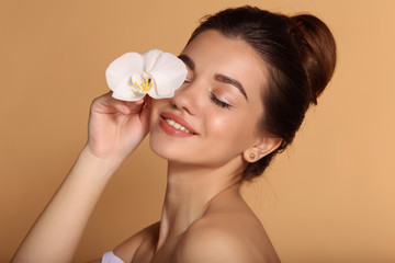 Obraz na płótnie Canvas Closeup portrait of young beautiful girl with flawless skin is holding white orchid flower in her hand. Skin care, beauty and cosmetics concept.
