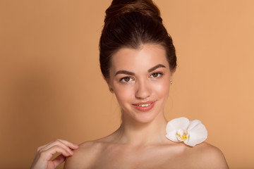Obraz na płótnie Canvas Closeup portrait of young beautiful girl with flawless skin with white orchid flower on her shoulder. Skin care, beauty and cosmetics concept.