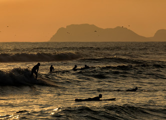 Scenic sunset moment with Silhouettes of surfers and seagulls on the  beach of the Pacific ocean. Lima, Peru. South America