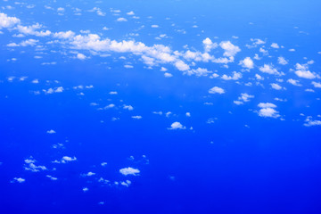 View of the window of airplane seeing  blue sky, white cloud and deep blue sea.