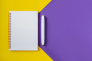 School notebook on yellow and purple minimalistic geometric background, spiral notepad on a table. Top view copy space, mockup. Office notepad flat lay.