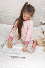 cute little girl drawing pictures while lying on bed. Kid painting at home