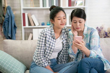 two teenager girl friends listening to music on sofa in living room at home. beautiful young women...