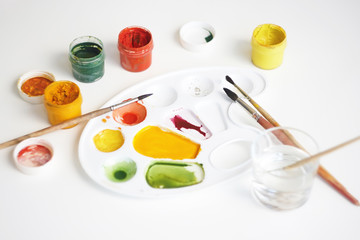 On a white background there is a still life with art supplies: gouache paints of different colors,...