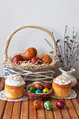Easter still life. Traditional Easter homemade Easter cakes with sweet icing and the colored eggs in wicker basket and on the wooden table. Close-up view, copy space, place for text, greeting postcard