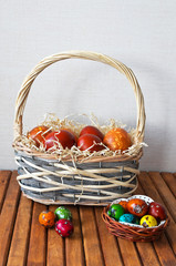 Traditional red painted Easter eggs in a wicker basket and small colorful quail eggs on a wooden table. Easter still life. Greeting card, close up, place for text, copy space