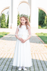 Portrait of cute little girl on white dress and wreath on first holy communion background church gate. first communion girl