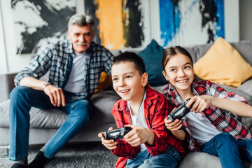 Two attractive teenage boy and girl are playing game console and smiling while sitting on the couch...