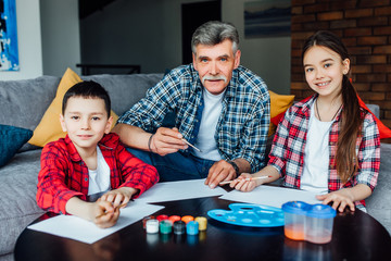 Fototapeta premium Portrait of cute girl and boy painting with colorful gouache with their grandfather.
