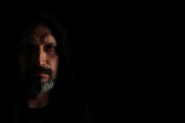 Brutal man with a gray beard in the hood with sharp shadows on a black background. Copy space.