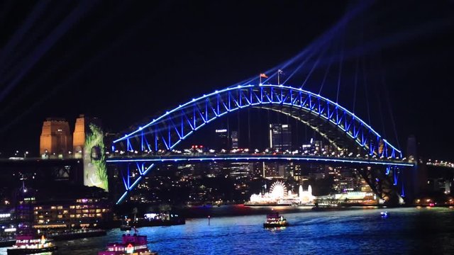Bright colours on the arch of Sydney Harbour bridge over waters of Harbour at night with blue laser beams of Vivid Sydney light show.