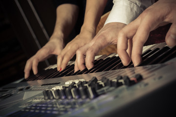 Fototapeta premium Four hands on the keys of the synthesizer shot with a shallow depth of field