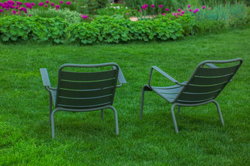 green chairs in the garden, dark green garden chairs for two on the green grass in front of flowers, spring relaxation in nature