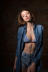 Fototapeta na wymiar Test shoot of an athletic brunette girl posing in lace bra and blue denim shirt in the shadows