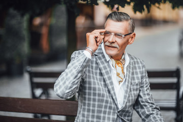 One local older senior man  businessman waiting sitting outside on break in stylish business office suit ,sunglasses