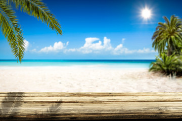 Wooden table background of free space and summer landscape of beach with palms and ocean. 