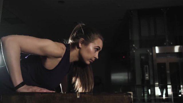young sports girl engaged in the evening in the gym. Does an exercise push-up from the bench.