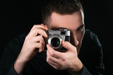 Fototapeta premium Man photographer holding a retro photo camera. Shooting process. Photographer looks at viewfinder.