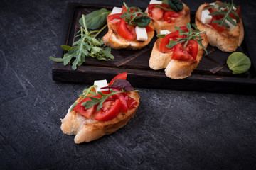 Bruschetta with tomatoes, mozzarella cheese and herbs on a cutting board in a dark background