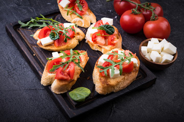 Bruschetta with tomatoes, mozzarella cheese and herbs on a cutting board in a dark background