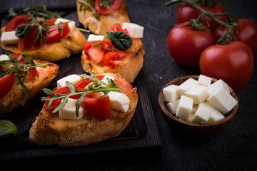 Bruschetta with tomatoes, mozzarella cheese and herbs on a cutting board in a dark background