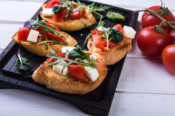 Bruschetta with tomatoes, mozzarella cheese and herbs on a cutting board in a white background