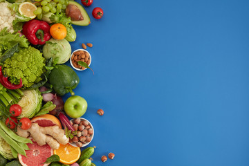 Obraz na płótnie Canvas Healthy food dish on blue background. Healthful set including vegetables and fruits. Grape, apple, kiwi, pepper, lime, cabbage, zucchini, grapefruit, ginger, nuts. Proper nutrition or vegetarian menu.