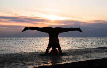 unrecognizable woman with beautiful body doing yoga headstand at sunrise on the sea, silhouette of yoga poses