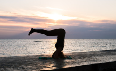 unrecognizable woman with beautiful body doing yoga headstand at sunrise on the sea, silhouette of yoga poses