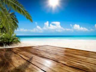 Wooden table background of free space and summer landscape of beach with palms and ocean. 