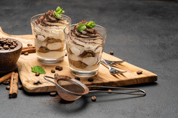 Classic tiramisu dessert in a glass on dark concrete background